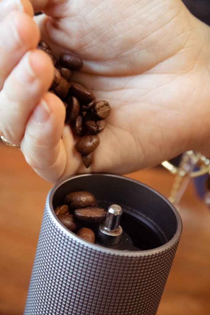 Kaffeebohnen rieseln aus der Hand in die Kaffeemühle rein.