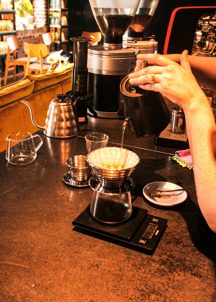 Kaffee wird frisch aufgebrüht. eine Glaskanne steht auf einer Waage, während in den Filter heißes Wasser gegossen wird.